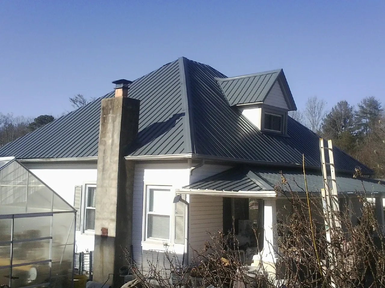 Dark blue standing seam metal roof on a white farmhouse with dormer — Slate & Tile Roof Repair by Roofing Brothers in Coalfield