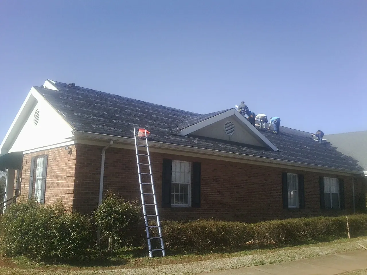 Crew tearing shingles off a brick ranch roof with a ladder set — Metal Roof Repair work by our crew in Coalfield