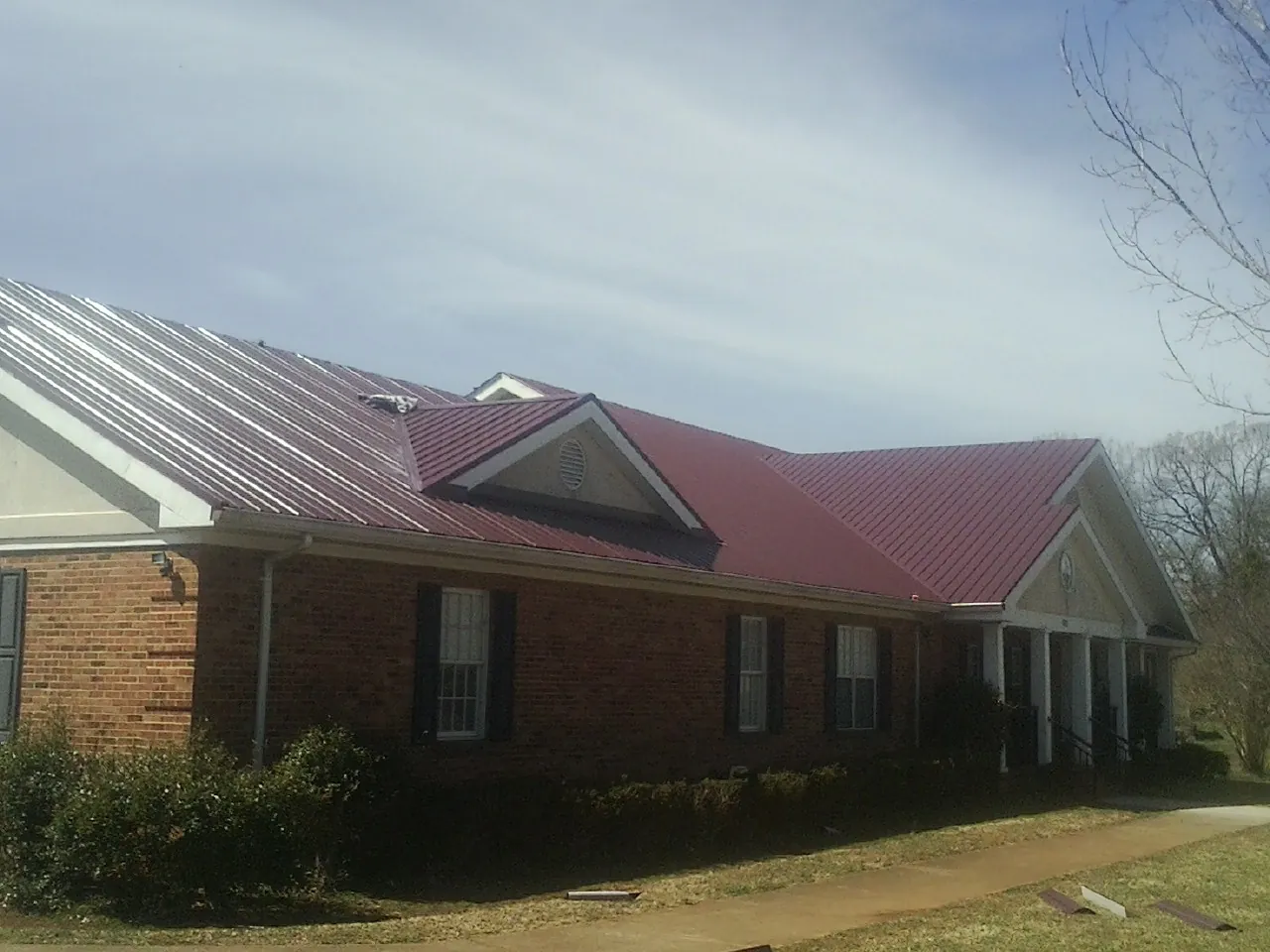 Red metal roof with gabled entries on a long brick building, from a Hail Damage Roof Repair job in Coalfield