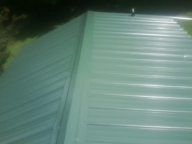 New green metal panels meeting at the ridge of a roof — Flat Roof Repair work by our crew in Coalfield