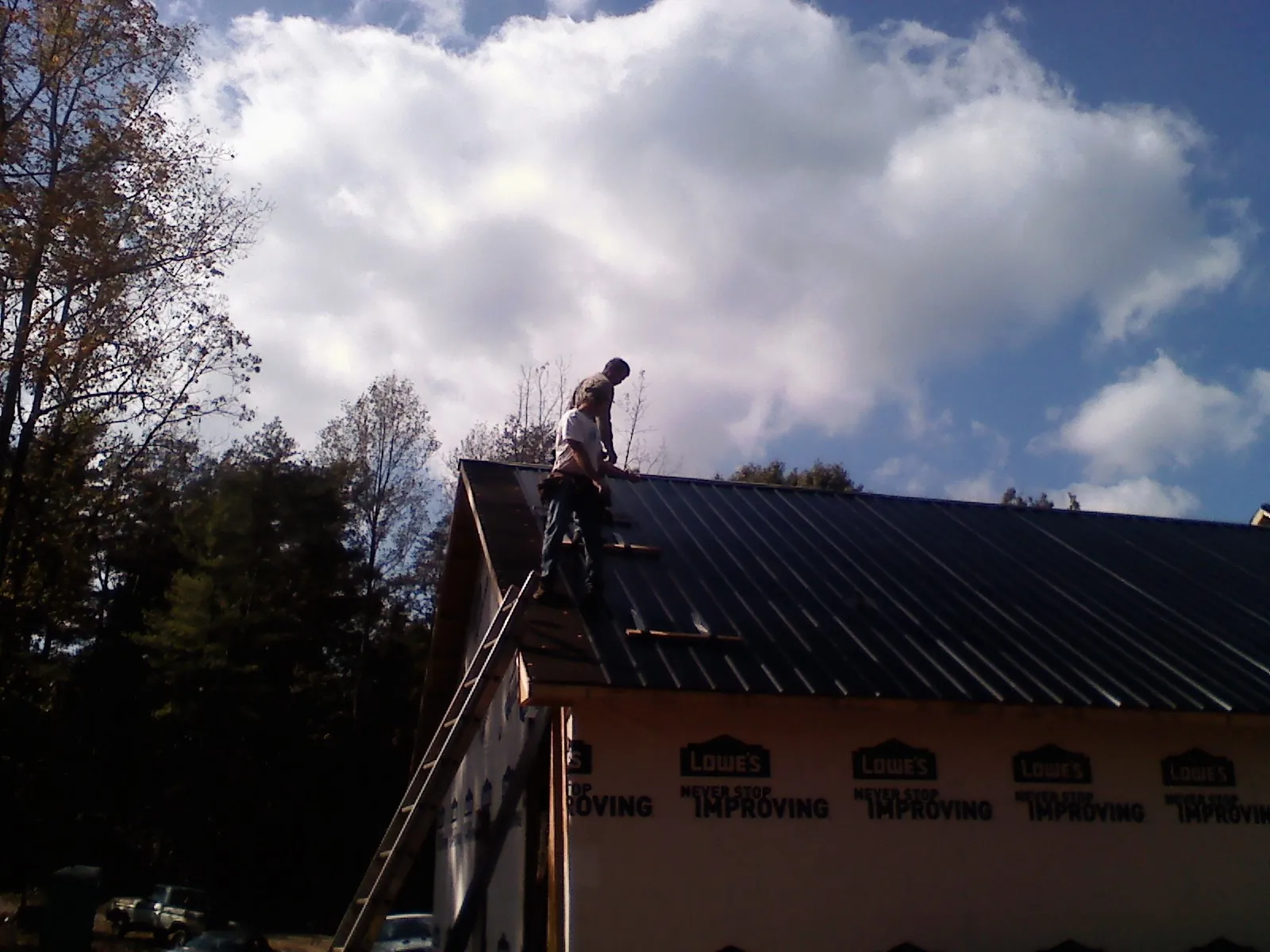 Roofer fastening dark metal panels high against a cloudy sky, from a Roof Inspection job in Coalfield