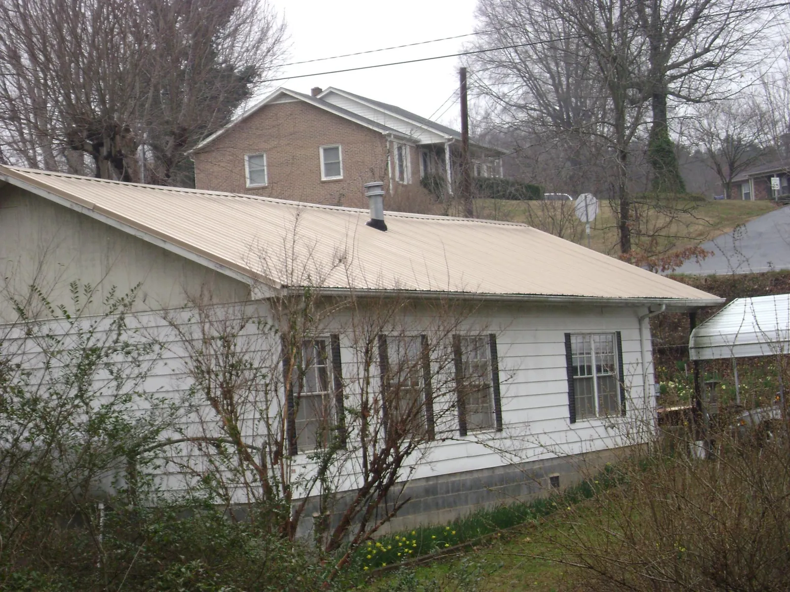 Tan metal roof on a white sided house set into a hillside — Commercial Roofing by Roofing Brothers in Coalfield